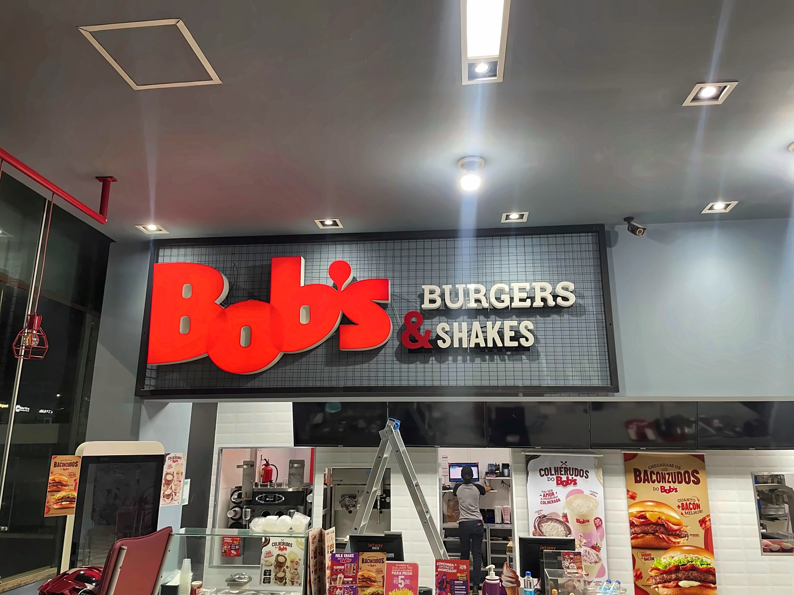 Letreiro iluminado Bob's Burgers & Shakes instalado sobre o balcão