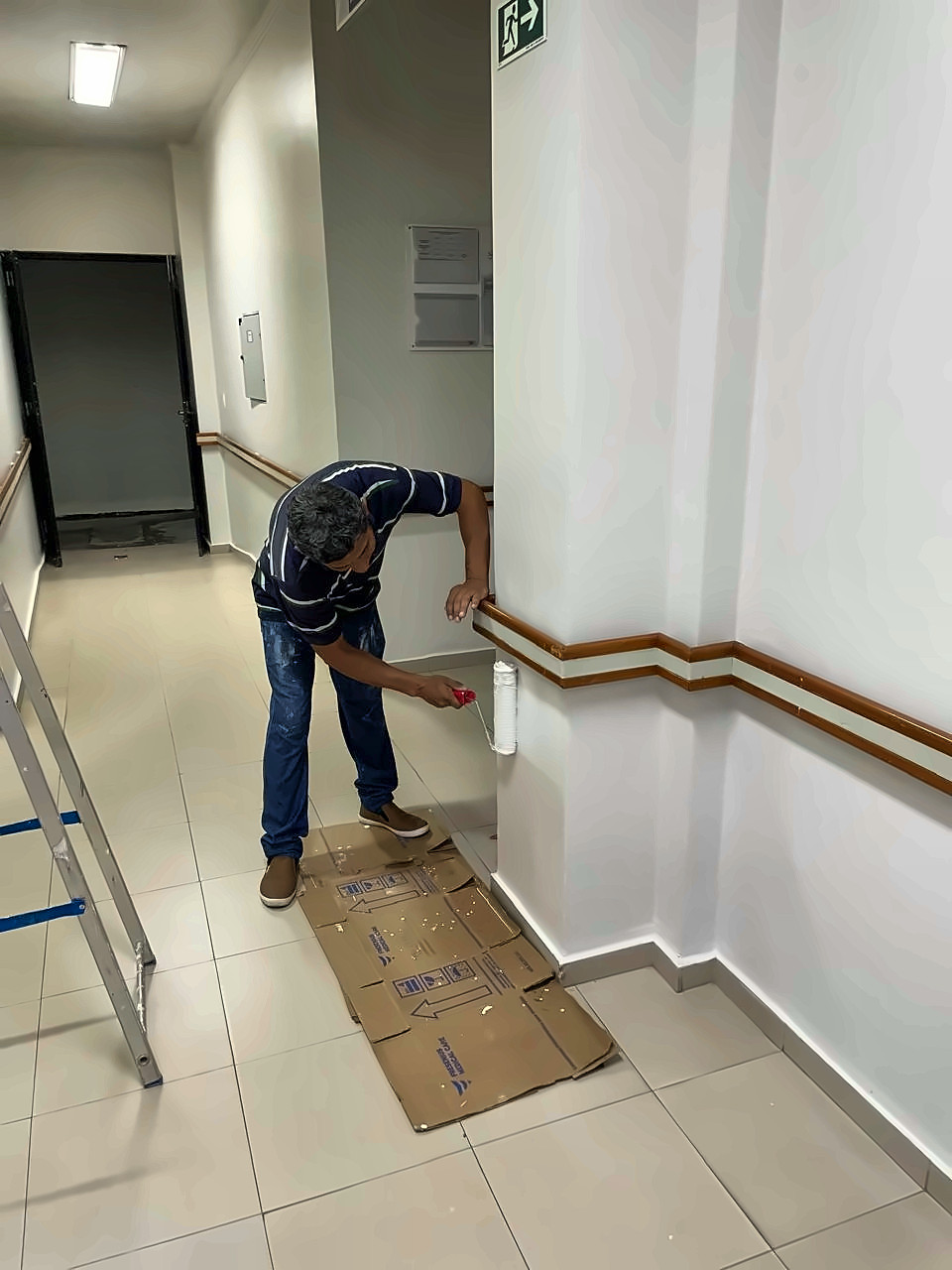 Pintor da Enobras aplicando tinta com rolo em parede de corredor